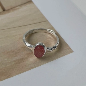 Detail of 925 silver adjustable ring with oval strawberry crystal on beige texture
