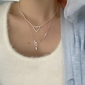 Detail of silver double-layered necklace with heart pendant and pearl on female model
