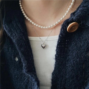 Detail showing a layered pearl necklace with a silver heart-shaped pendant on a model