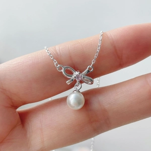 Detailed view of silver bow necklace with pink diamond and hanging white pearl