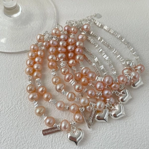 Gros plan de perles d'eau douce roses et d'un pendentif coeur en argent sur gourmette