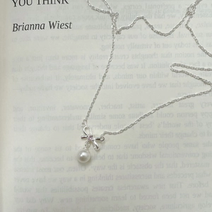 Detail of S925 silver bow pendant with pink zircon and white pearl on a book background