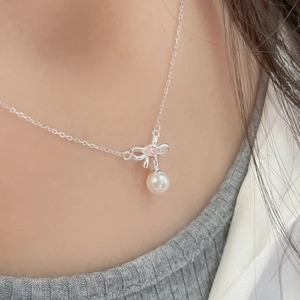 Detail of silver bow pendant necklace with pink diamond and white pearl on neck