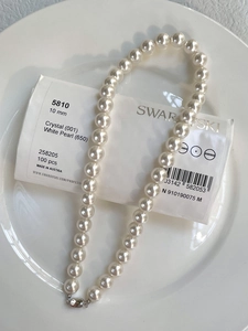 Macro detail of 10mm crystal white pearl necklace with silver clasp on ceramic plate