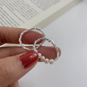 Detail of s925 silver beaded rings and white round pearls on a female hand