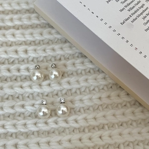 Detail of two pairs of white pearl stud earrings on a warm knitted sweater background
