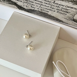 Macro view of minimalist white pearl earrings with silver needles on jewelry box