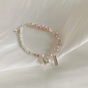 Vue macro d'un bracelet en perles d'argent S925 avec breloque cœur sur soie blanche