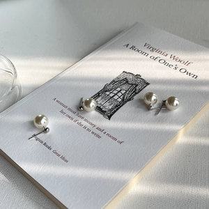 Close-up of elegant pearl stud earrings displayed on a book with artistic window shadows