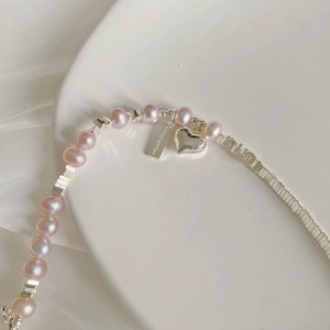 Détail macro du bracelet en perles roses avec breloque cœur et étiquette gravée