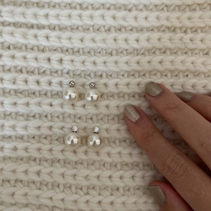 Detailed macro view of minimalist pearl stud earrings with zircon inlay on white knit fabric