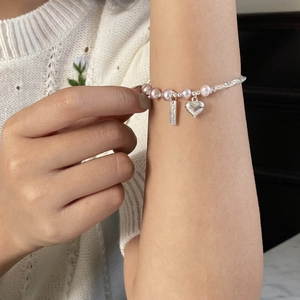 Détail d'un bracelet avec perles roses et breloque en cœur argenté porté au poignet