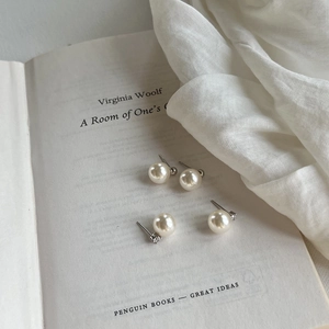 Close-up of minimalist white pearl stud earring set on an open book background