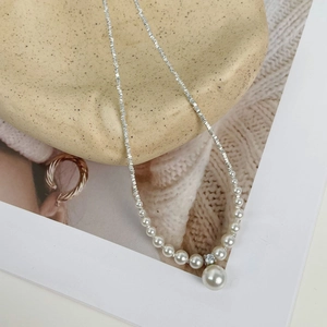 Detail view of silver crushed bead necklace with white pearls on a ceramic plate