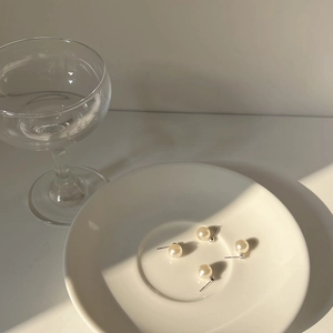 Close-up of minimalist white faux pearl stud earrings with 925 sterling silver pins on a dish