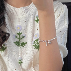 Gros plan d'un bracelet en perles roses avec pendentif cœur au poignet d'une femme