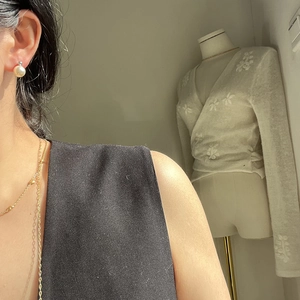 Close-up of elegant gold chain necklace and creamy white pearl stud earring on a model