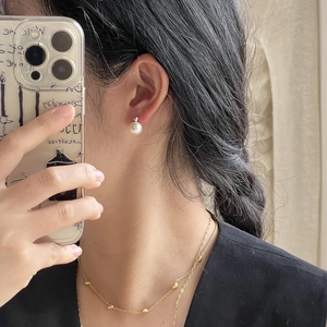 Close-up of elegant white pearl stud earrings and gold heart chain necklace on model