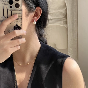 Close-up of elegant pearl stud earrings and layered gold necklace on a model