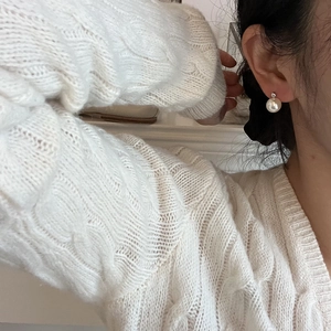 Close-up of elegant white pearl stud earrings worn with a warm white knit sweater