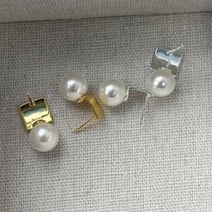 Detailed close-up of square metal stud earrings with elegant round white pearls