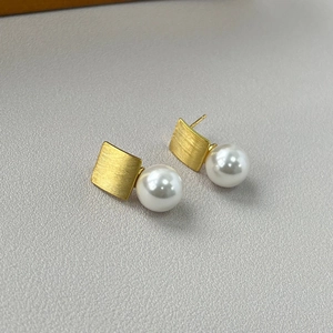 Detail of square brushed gold metal and round white pearl on elegant vintage earrings