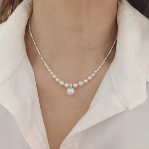 Macro shot of a gradient white pearl necklace with zircon pendant on a white shirt