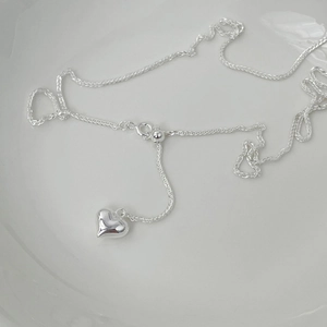 Detail of adjustable S925 sterling silver long heart pendant necklace on ceramic plate