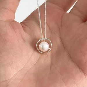 Irregular hollow silver necklace with round white freshwater pearl pendant shown in hand