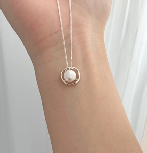Detail of hollow silver pendant with natural freshwater pearl on delicate chain worn on wrist