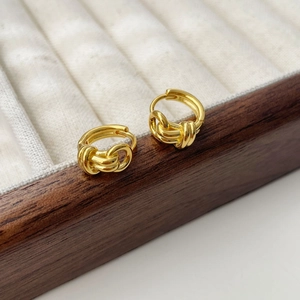 Close-up of golden minimalist double-layer twisted knot hoop earrings in a wooden jewelry box