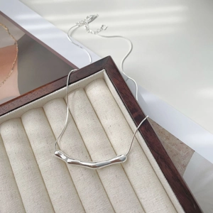 Macro detail of silver minimalist necklace featuring an irregular fluid pendant on tray