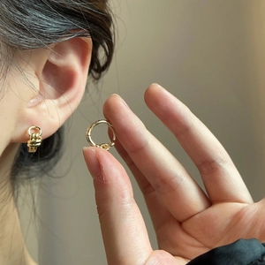Detail of gold double-layer twisted knot hoop earrings worn by a model in soft light