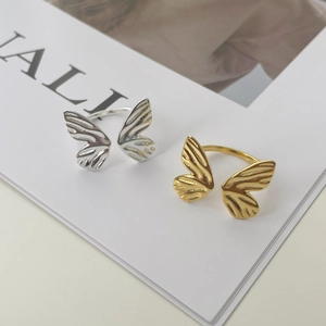 Detailed view of silver and gold butterfly open rings with fine wing textures on a white page