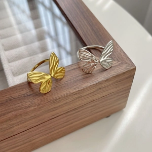 Close-up of gold and silver butterfly rings with textured wings on wood box