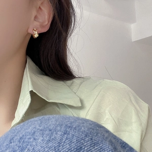 Detailed close-up of a twisted knot geometric gold-plated earring on a female model
