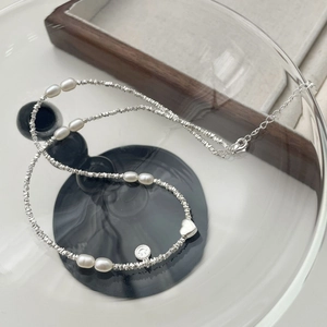Dettaglio di ciondoli a cuore e sorriso su collana di perle irregolari e argento