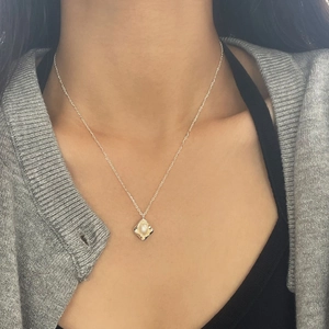 Detail of a square metal pendant necklace featuring a round white pearl on a model