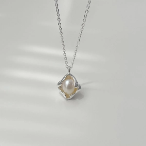 Macro detail of irregular silver pendant with white pearl on minimalist necklace