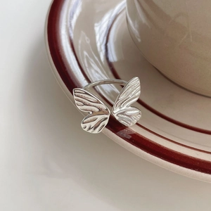 Macro detail of S925 sterling silver butterfly ring with textured wings on ceramic plate