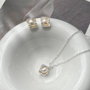 Detail shot of irregular silver jewelry set with pearls on white ceramic dish