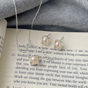Detailed view of S925 silver necklace and pearl earrings set on vintage book pages