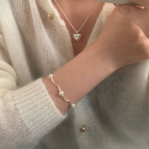 Detail of 925 sterling silver heart necklace and wavy pearl bracelet on a knit cardigan