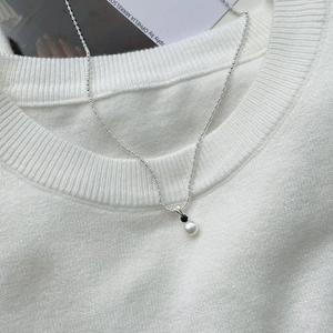 Detail of S925 silver pearl necklace with black cubic zirconia on white knit sweater