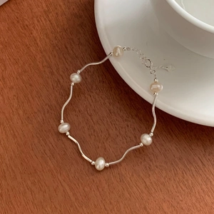 Detail of S925 silver wave bracelet with freshwater pearls on a cozy wooden desk