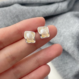 Detail of square silver studs with faux pearl inlay held against a grey knit fabric background