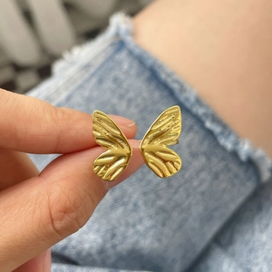 Close-up of golden butterfly ring showing detailed wing texture on denim background