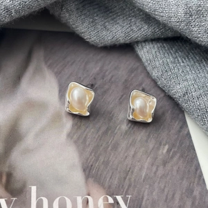 Detailed shot of irregular square silver studs with white pearls on a display card