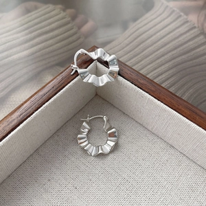 Detailed macro view of silver hoop earrings featuring a unique wavy pleated texture