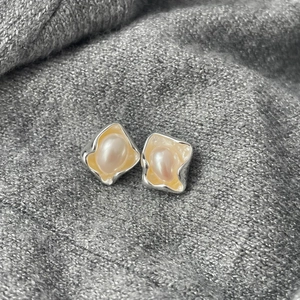 Detailed close-up of baroque pearls in irregular silver frames on a grey knit texture